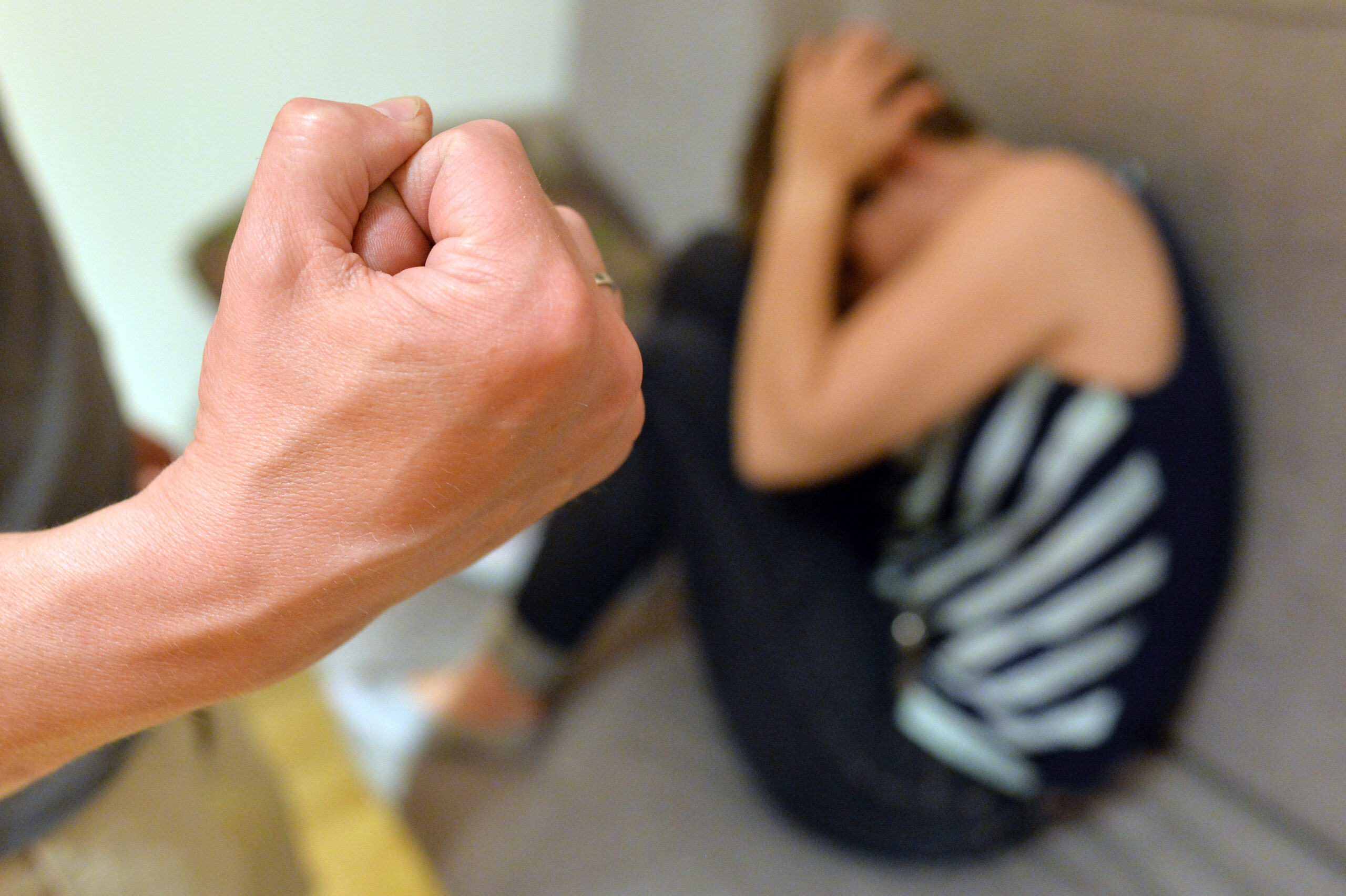 Die Hand eines Mannes ist zu sehen, in der Ecke kauert eine Frau