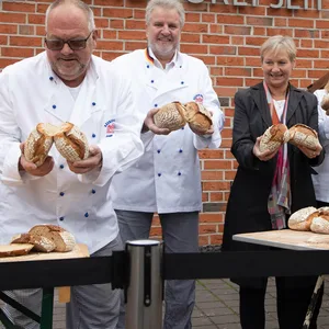 Die fünf Personen brechen das Doppelbrot und halten es in die Kamera.