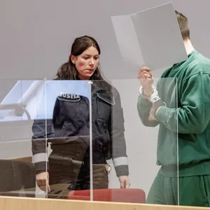 Ein Angeklagter in grünem Jogginganzug wird von zwei Justizbeamten in den Gerichtssaal geführt