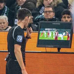 Schiedsrichter Matthias Jöllenbeck steht am VAR-Bildschirm und guckt sich die strittige Szene an.