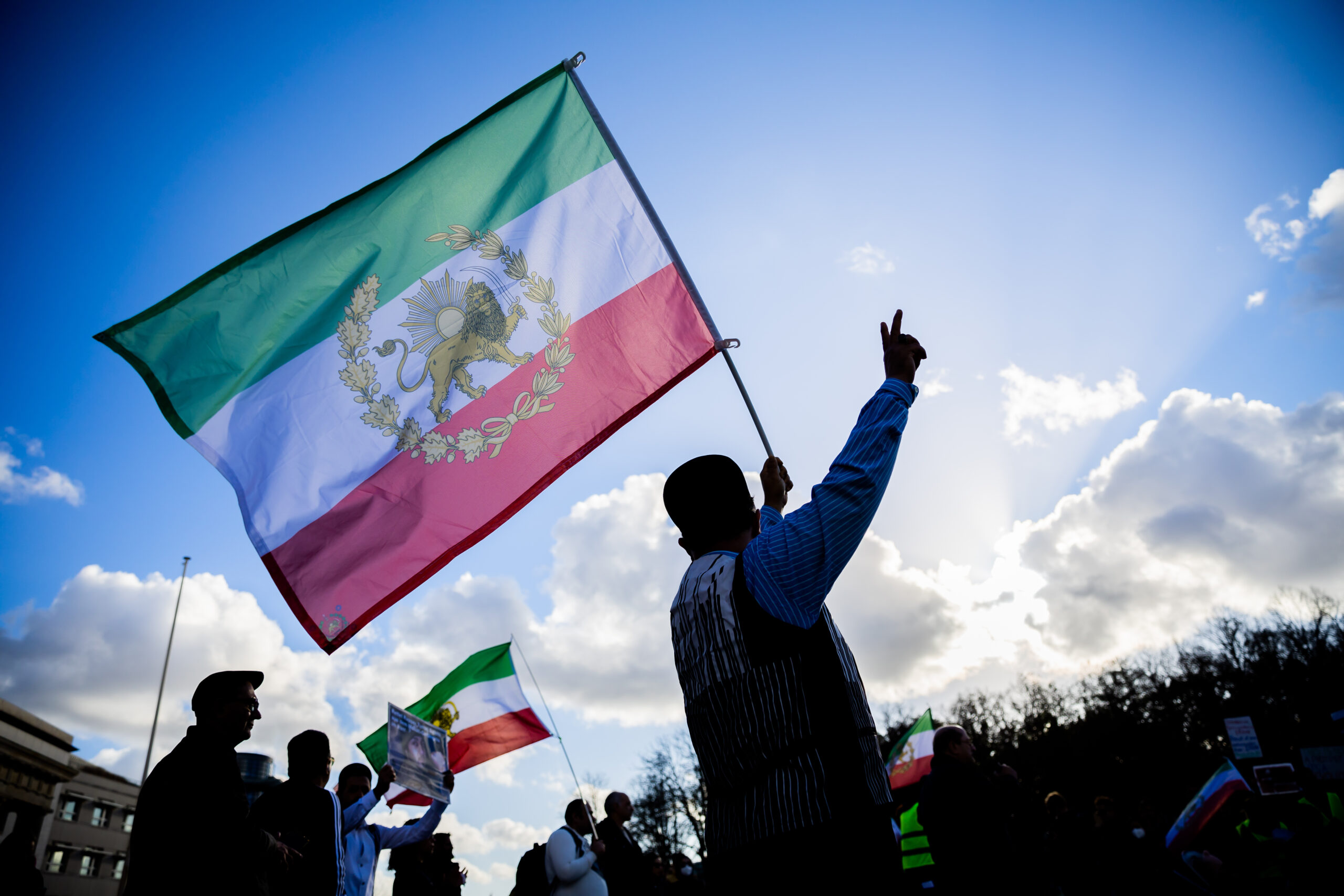 Ein Demonstrant schwenkt am Brandenburger Tor eine iranische Flagge und zeigt das «Victory»-Zeichen.