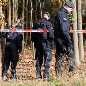 Polizisten hinter einem Polizeiabsperrband durchsuchen das Gelände.