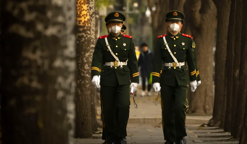 Chinesische paramilitärische Polizisten mit medizinischen Masken gehen in Formation eine Straße in Peking entlang.