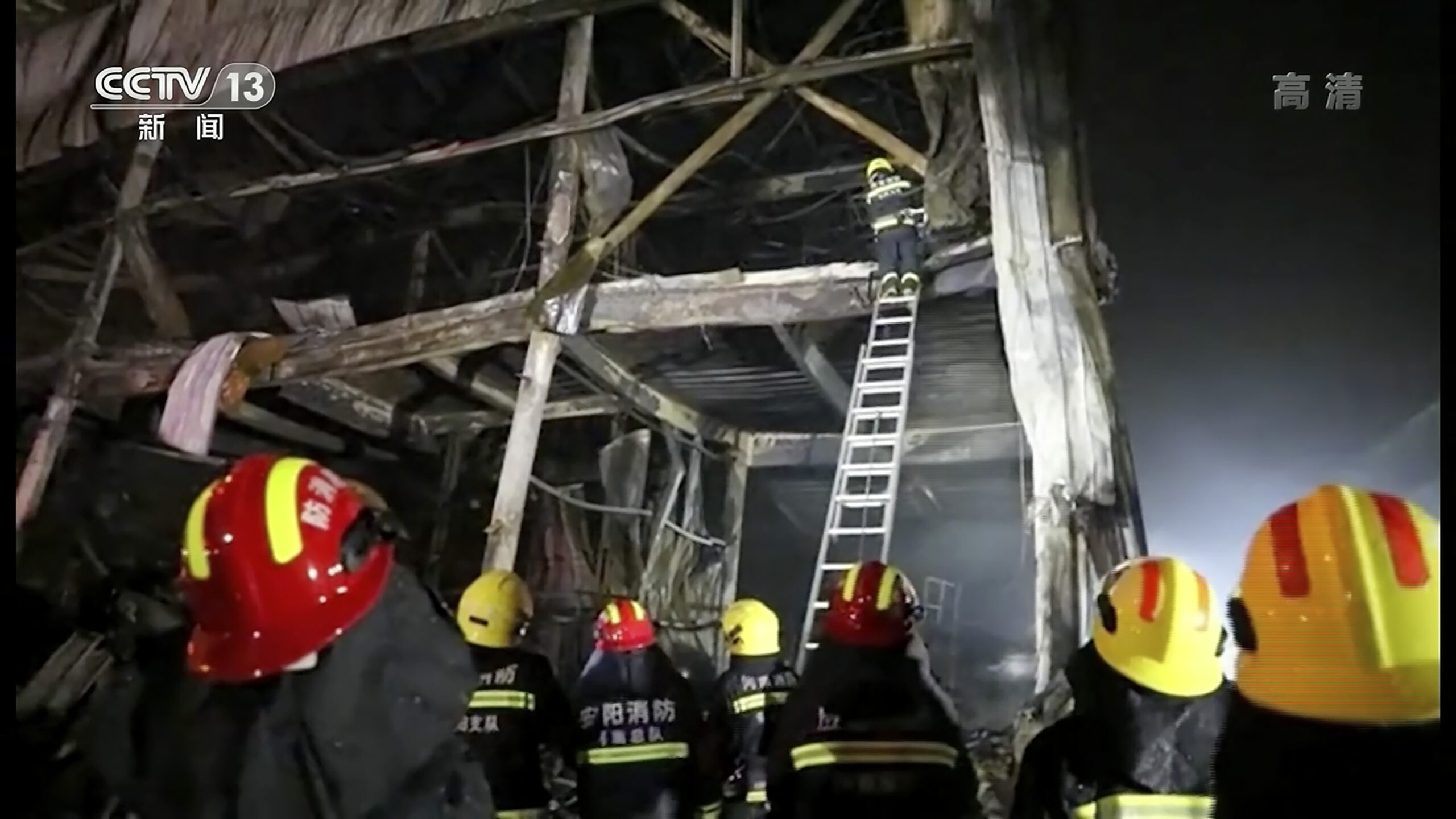 Rettungskräfte klettern mit einer Leiter in die Überreste der abgebrannten Fabrik.