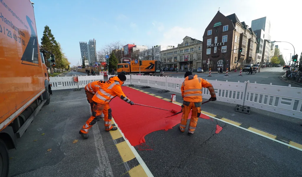 Straßenarbeiter färben den Radweg auf der Reeperbahn rot ein