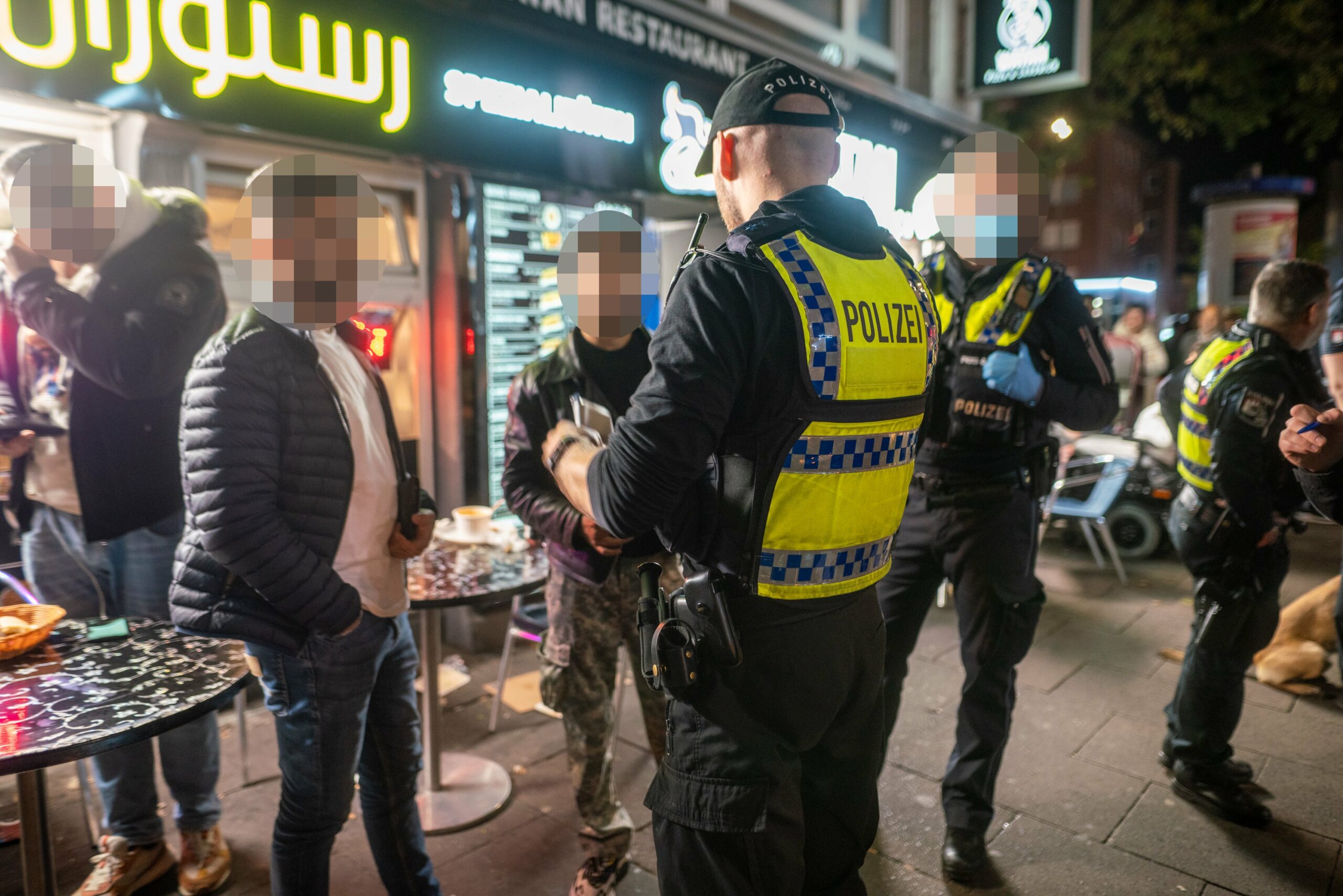 Polizisten sprechen mit Männern vor einem Imbiss in St. Georg, wo eine Razzia stattfand