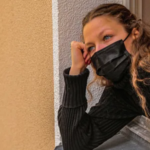 Eine junge Frau mit Maske schaut aus dem Fenster.