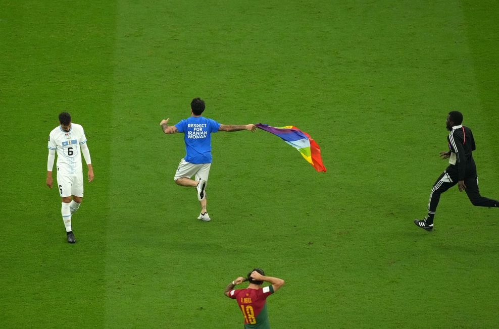 Ein Mann läuft mit T-Shirt und Regenbogen-Fahne über das Spielfeld.