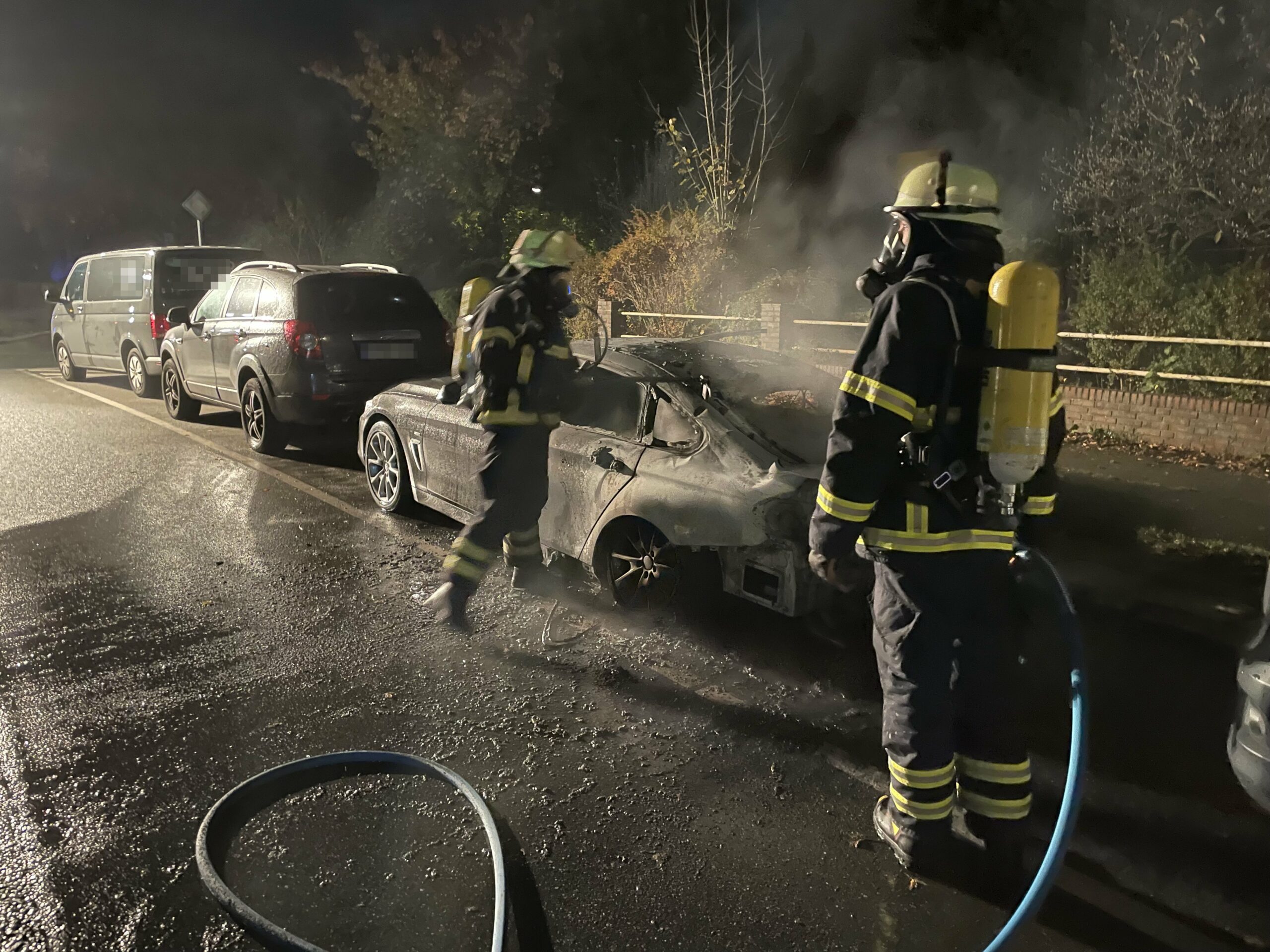 Feuerwehrleute löschen einen BMW am Straßenrand in Rahlstedt