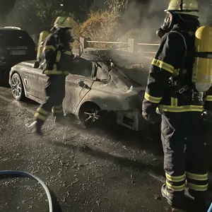 Feuerwehrleute löschen einen BMW am Straßenrand in Rahlstedt
