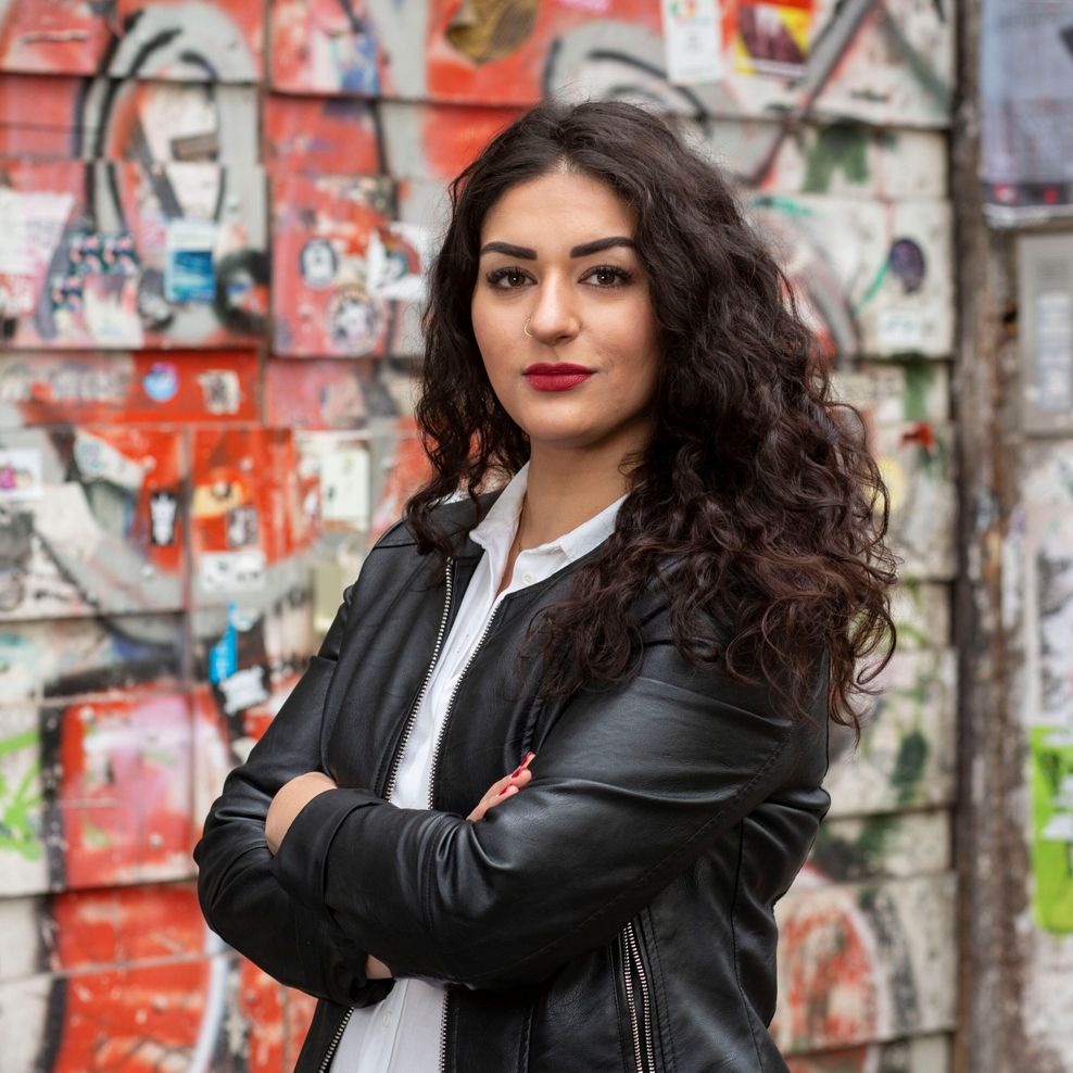 Cansu Özdemir steht in Lederjacke vor einer bunten Wand.