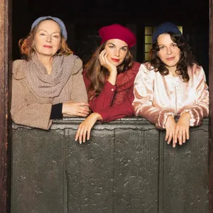 Drei Frauen in der Kulisse, sie stehen hinter einer halboffenen Stalltür eines Fachwerkhauses
