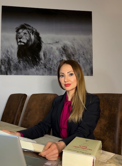 Jacqueline Ahmadi sitzt an einem Tisch vor einem Bild von einem Löwen.