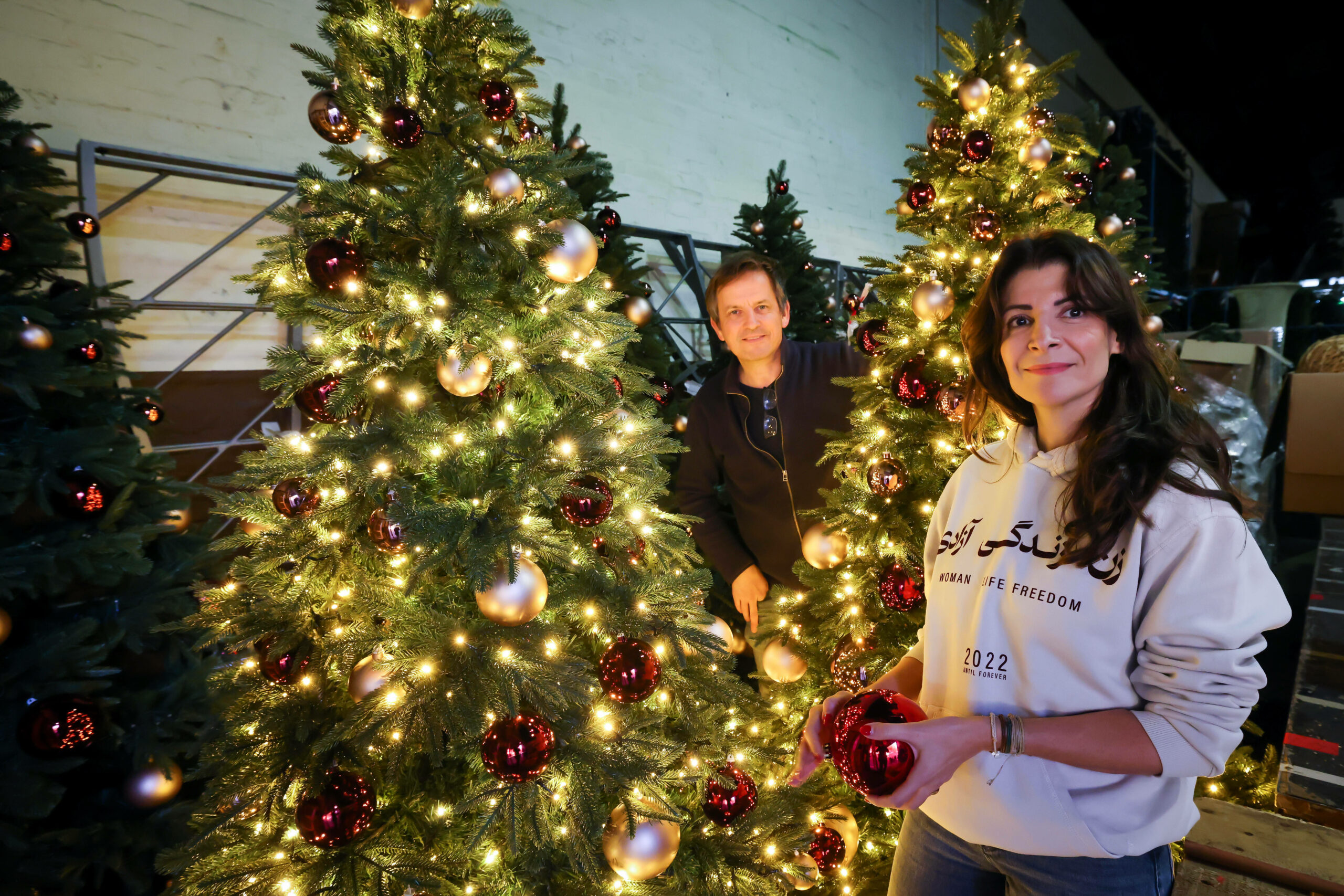 Nasi Bostak (r.) und Marcel Klöpner von „Die Schmücker - Lichtprojekte und Dekoration“, stehen zwischen leuchtenden Kunst-Weihnachtsbäumen in ihrem Lager.