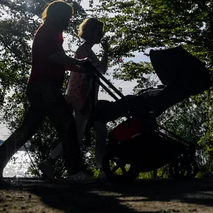 Zwei Frauen schieben einen Kinderwagen durch die sonnendurchfluteten Parkanlagen an der Außenalster.