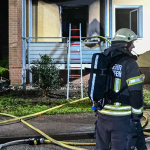 Feuerwehrleute stehen vor der ausgebrannten Wohnung