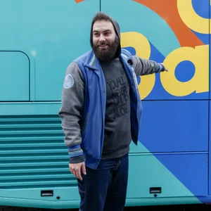 Dominik Blog steht vor einem Duschbus und zeigt auf das Logo.