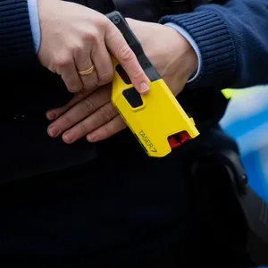 Ein Polizist mit einem Taser in der Hand vor einem Polizeiwagen