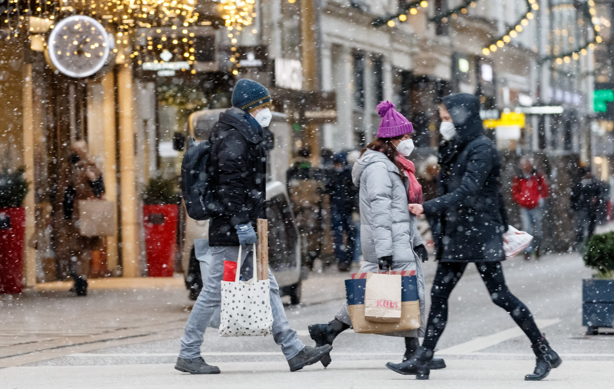 Passanten gehen am Tag vor Weihnachten mit Einkaufstaschen bei leichtem Schneefall durch die Hamburger Innenstadt.