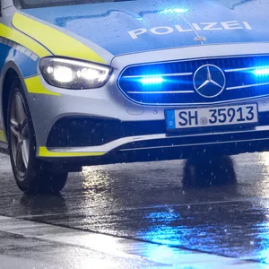 Ein Streifenwagen steht mit Blaulicht auf der regennassen Straße. (Symbolbild)