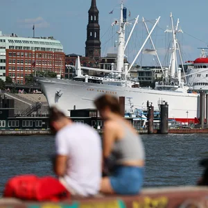 Menschen sitzen am Hafen auf einer Mauer