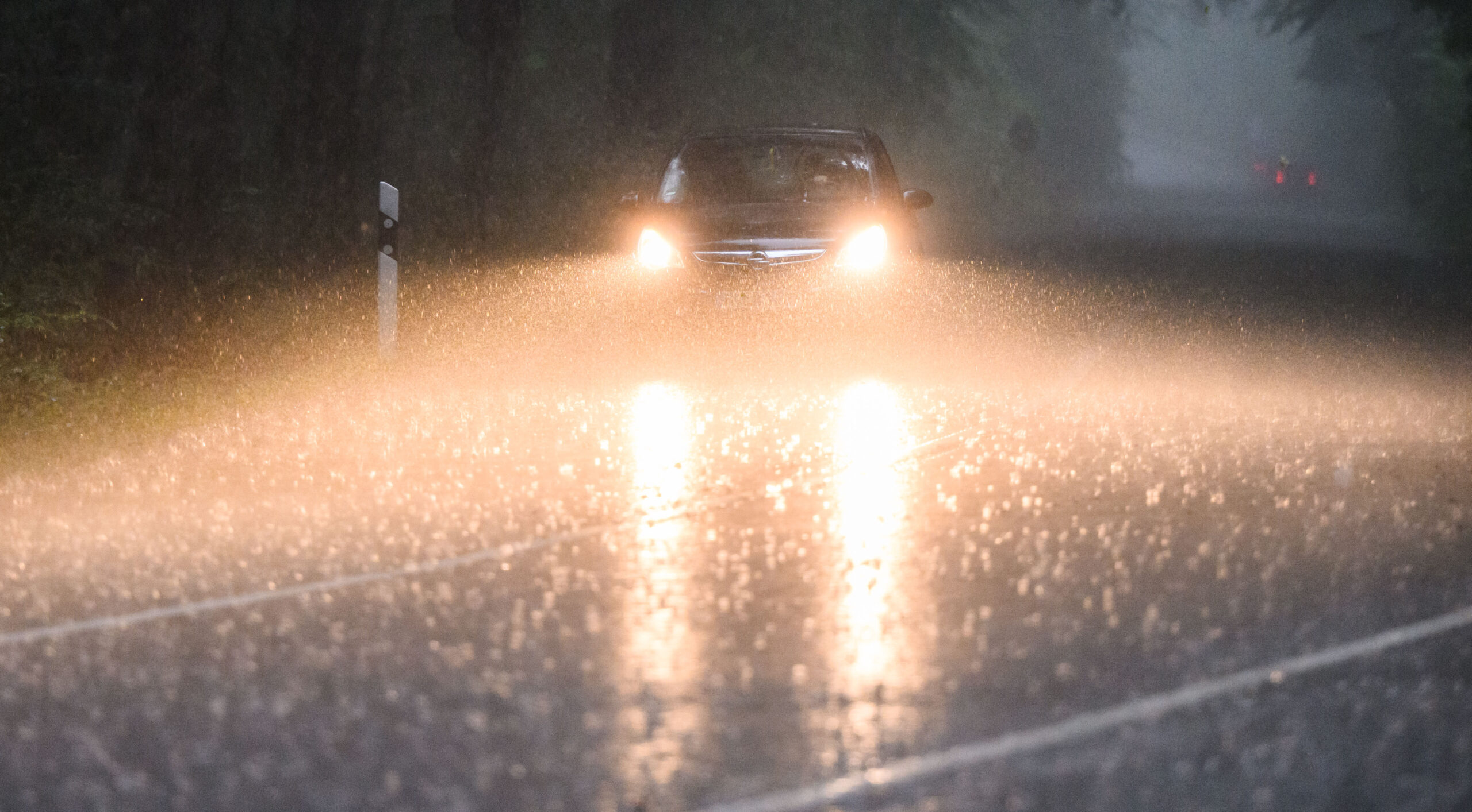 Ein Auto fährt während eines Gewitters mit Starkregen über eine Landstraße