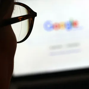 Die Seite der Suchmaschine von Google ist hinter einer Frau mit Brille zu sehen.