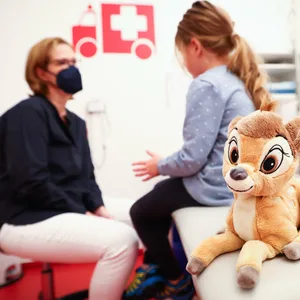 Eine Kinderärztin (l) spricht vor einer Untersuchung mit ihrer jungen Patientin, während deren Mutter daneben steht.