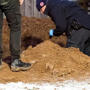 Ermittler der Polizei arbeiten hinter einem Mehrfamilienhaus in einem Garten an einem Erdloch. Dort wurde am Mittag eine vergrabene Leiche gefunden