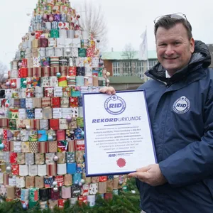 RID-Rekordrichter Olaf Kuchenbecker hält die Urkunde vor den größten Weihnachtsbaum aus Konservendosen auf dem Kirchplatz vor dem Michel.