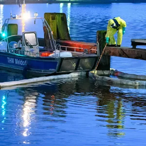 Einsatzkräfte des THW in Schutzanzügen arbeiten mit Ölschlengeln an einem Steg.