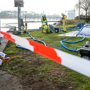 Einsatzkräfte des THW arbeiten in Schutzanzügen nahe des Kanals.