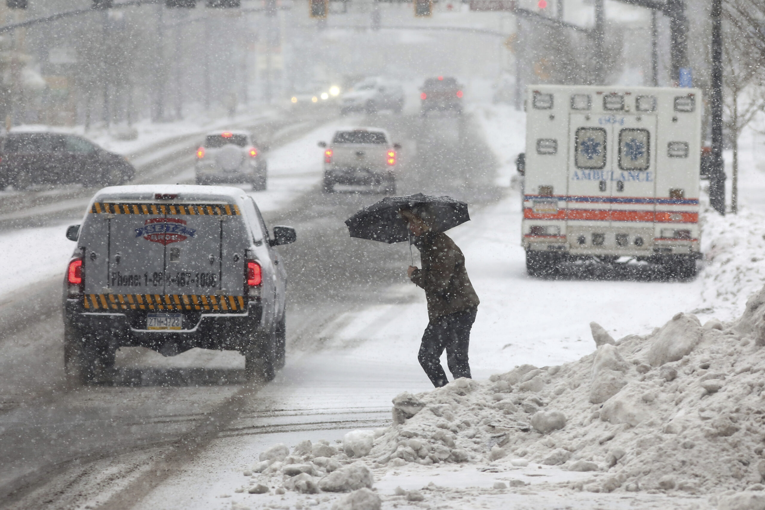 Eine Person überquert eine Straße, während sie sich mit einem Regenschirm vor dem beginnenden Schneefall schützt.