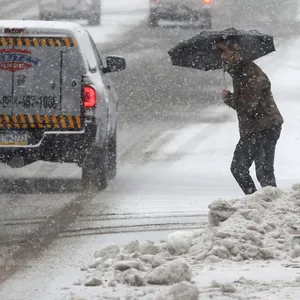 Eine Person überquert eine Straße, während sie sich mit einem Regenschirm vor dem beginnenden Schneefall schützt.