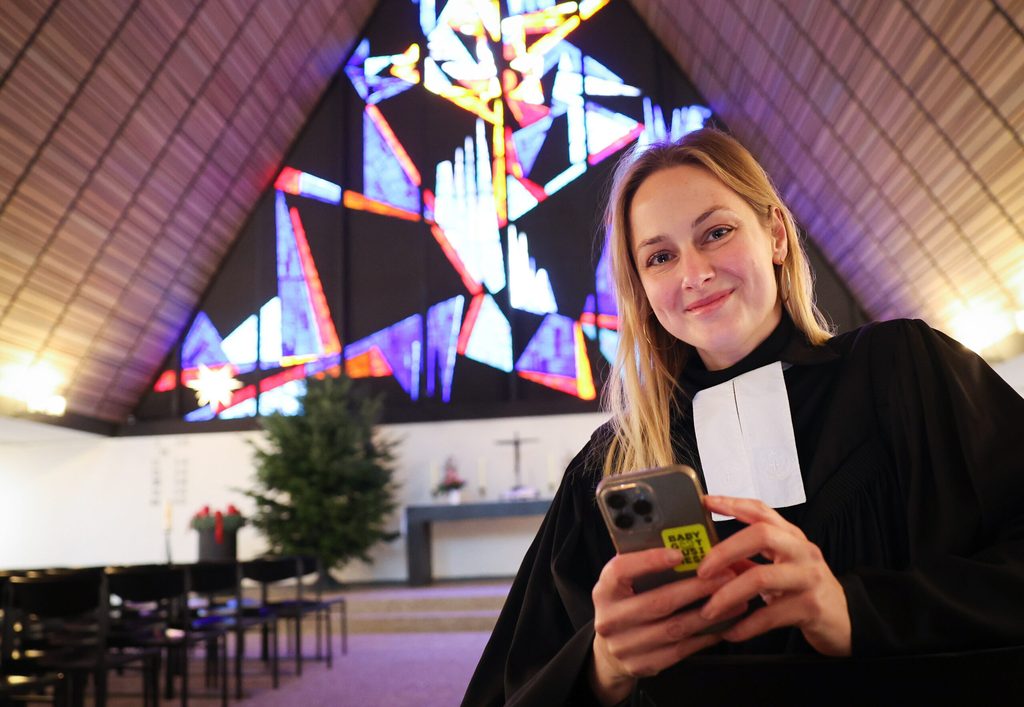 Die Pastorin steht mit ihrem Handy in der Hand in der Kirche