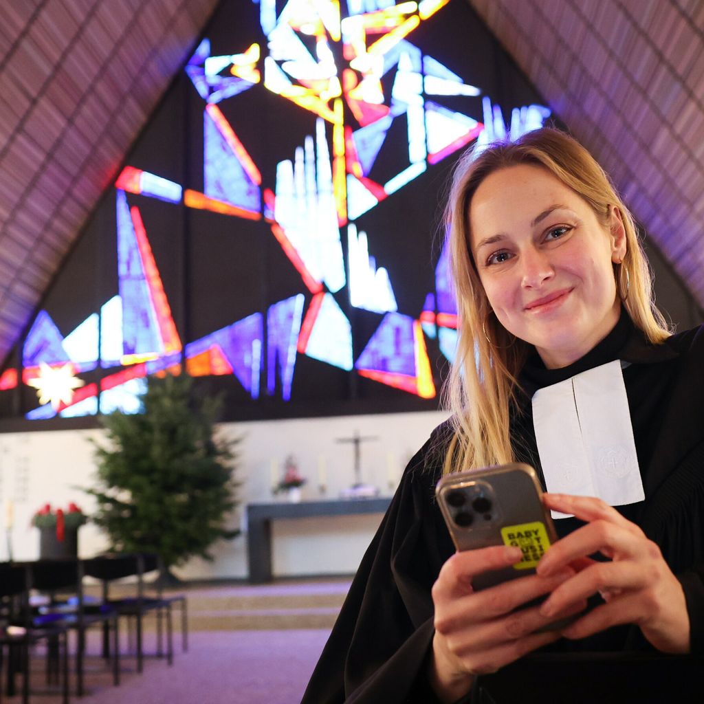 Die Pastorin steht mit ihrem Handy in der Hand in der Kirche