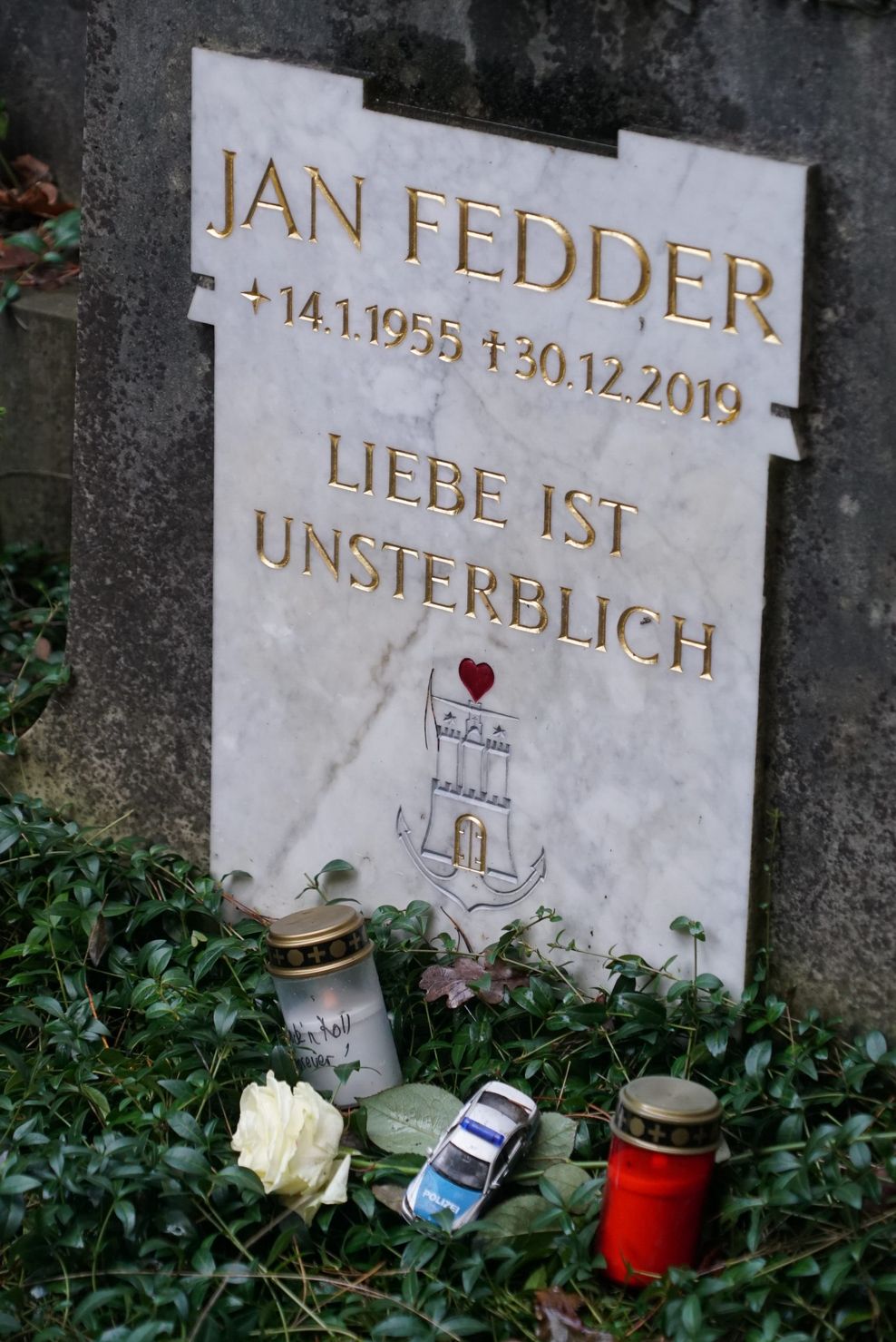 Ein kleines Polizeiauto und eine Rose liegen auf Jan Fedders Grab in Ohlsdorf