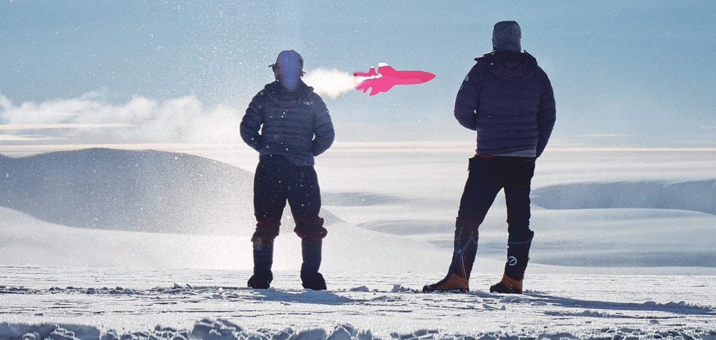 Zwei Männer stehen im Schnee und blicken auf einen rosa Jet.