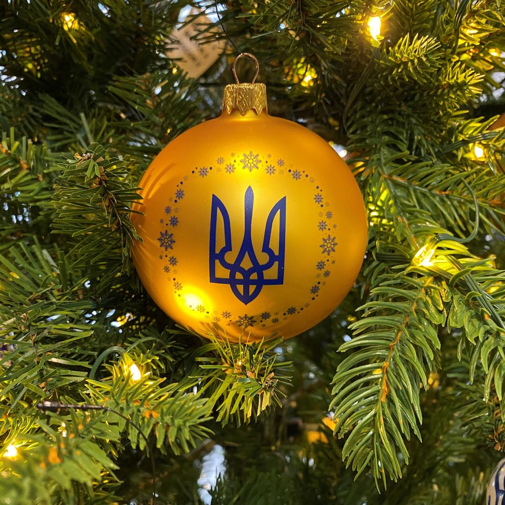 An einem geschmückten Baum in einem Geschäft hängt eine Kugel in den ukrainischen Nationalfarben Blau und Gelb mit dem Dreizack als Wappen.