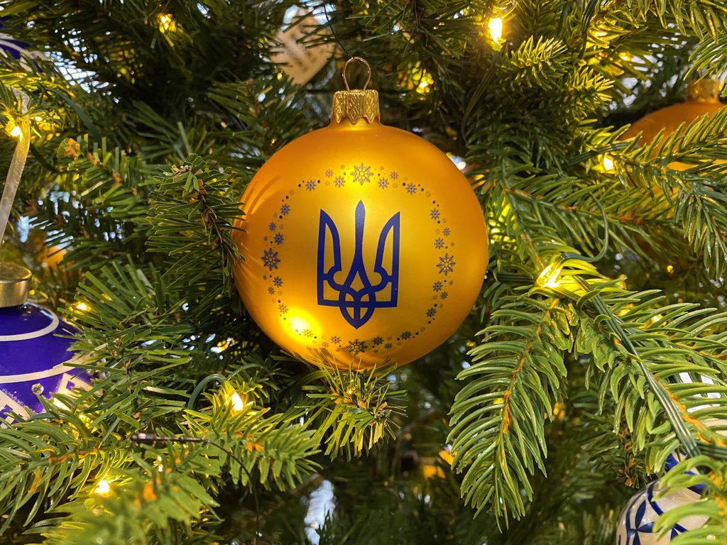 An einem geschmückten Baum in einem Geschäft hängt eine Kugel in den ukrainischen Nationalfarben Blau und Gelb mit dem Dreizack als Wappen.