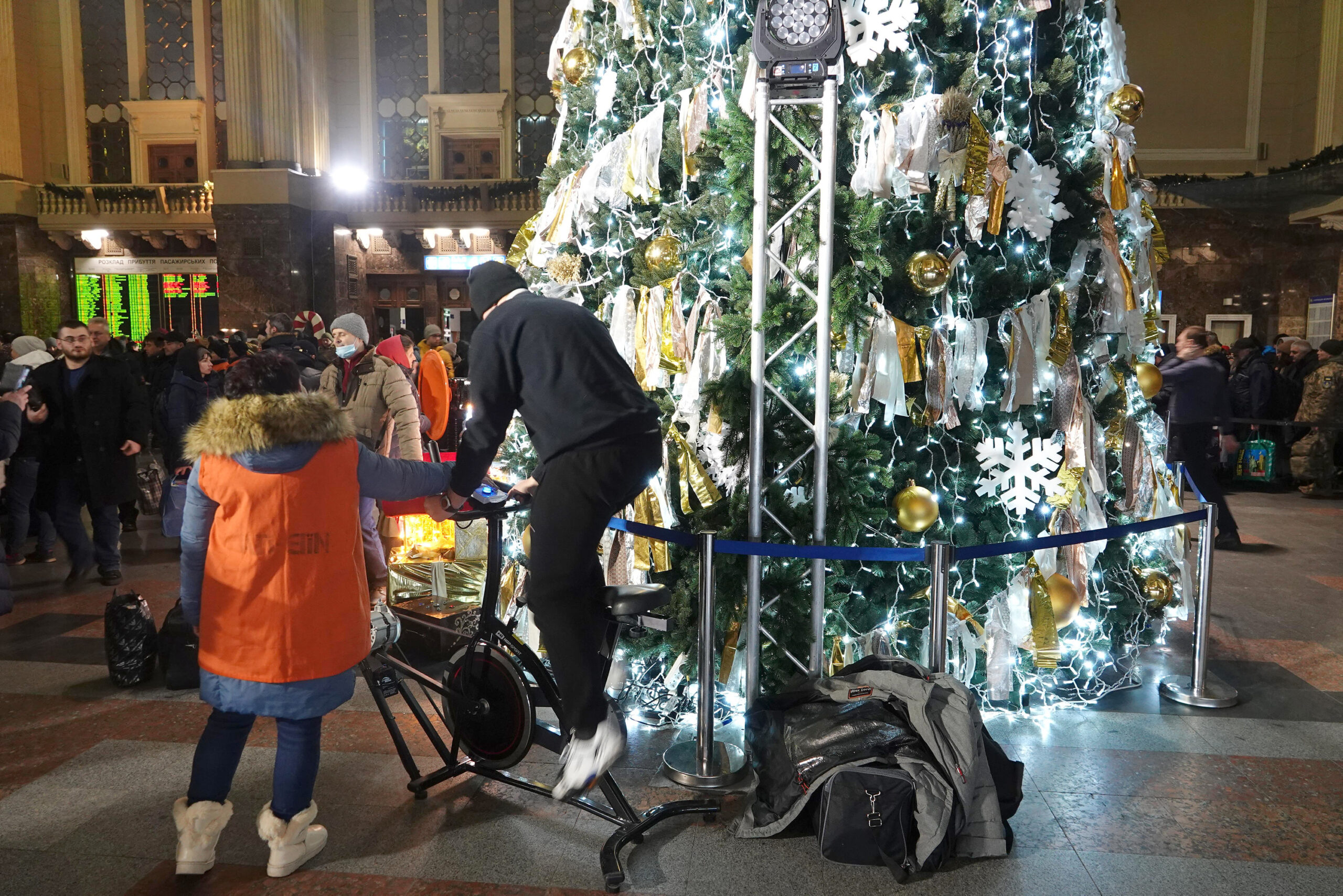 In der Empfangshalle auf dem Hauptbahnhof tritt ein Mann auf einem Energie-Fahrrad in die Pedalen, um den geschmückten Baum zum Leuchten zu bringen.