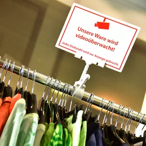 Kleiderstange mit Kleidung in einem Geschäft mit dem Hinweisschild: „Unsere Ware wird videoüberwacht!“