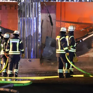 Feuerwehrleute bekämpfen die in der Halle lodernden Flammen.