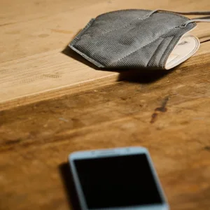Eine FFP2-Maske liegt neben einem Handy an einem Arbeitsplatz.