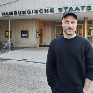 Kratzer, schwarz gekleidet mit Basecap, vor der Staatsoper