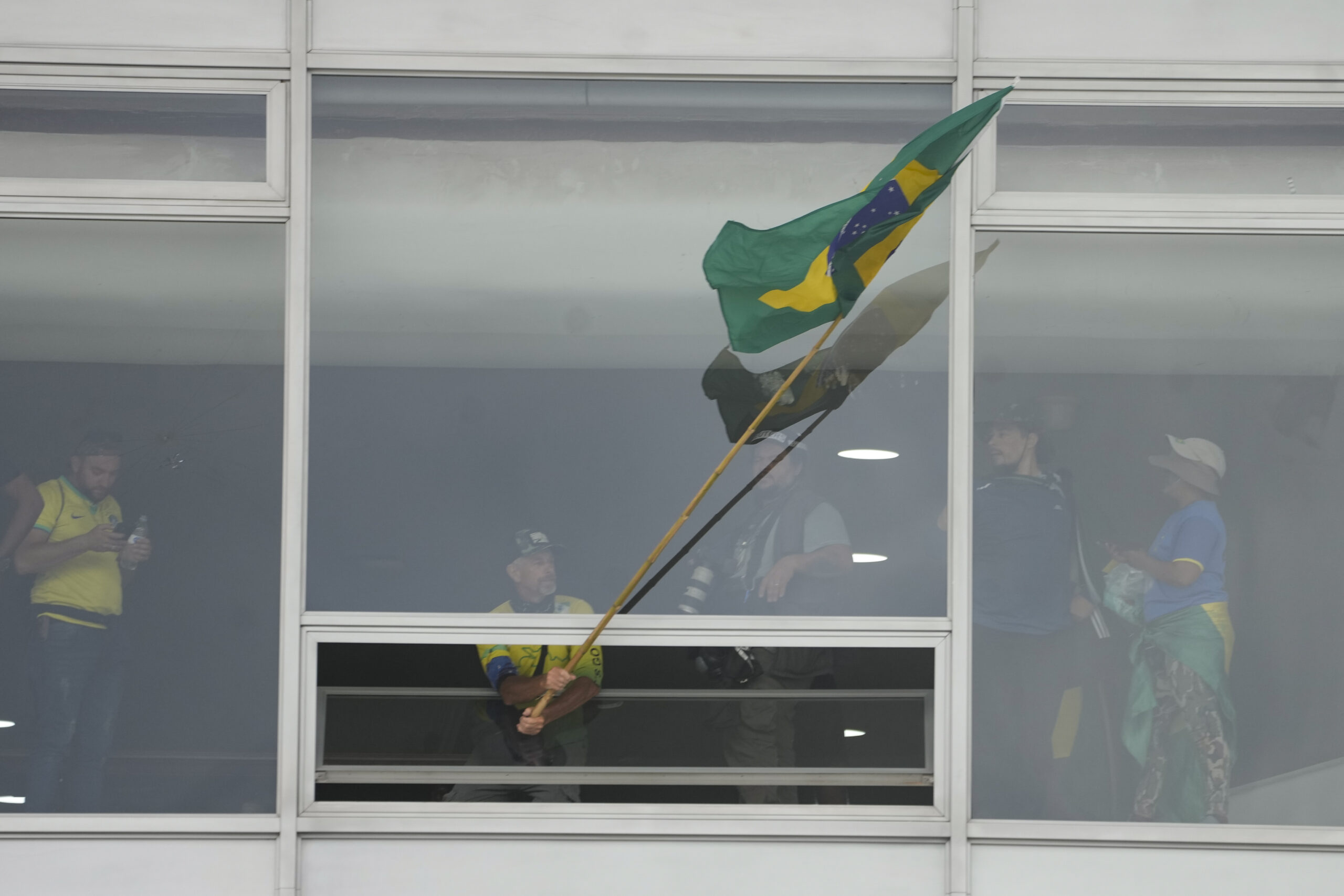 Ein Anhänger des ehemaligen brasilianischen Präsidenten Bolsonaro schwenkt eine brasilianische Nationalfahne aus einem Fenster des Palacio do Planalto, den offiziellen Sitz des brasilianischen Präsidenten.