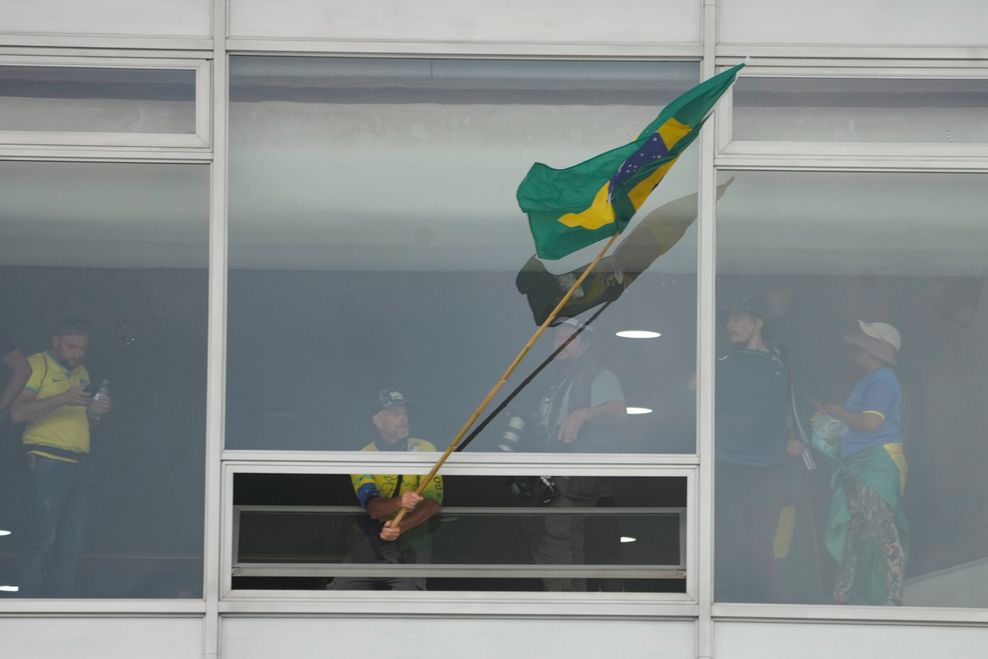 Ein Anhänger des ehemaligen brasilianischen Präsidenten Bolsonaro schwenkt eine brasilianische Nationalfahne aus einem Fenster des Palacio do Planalto, den offiziellen Sitz des brasilianischen Präsidenten.