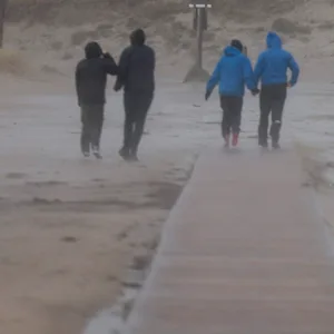 Strandbesucher:innen in St. Peter-Ording kämpfen sich durch die Orkanböen.
