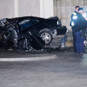 Ein zerstörter PKW liegt zwischen zwei Säulen des Brandenburger Tors. Daneben stehen Einsatzkräfte der Polizei.