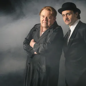 Links Wöhler in schwarzem Mantel, rechts Rotschopf im Anzug. Im Hintergrund Nebel